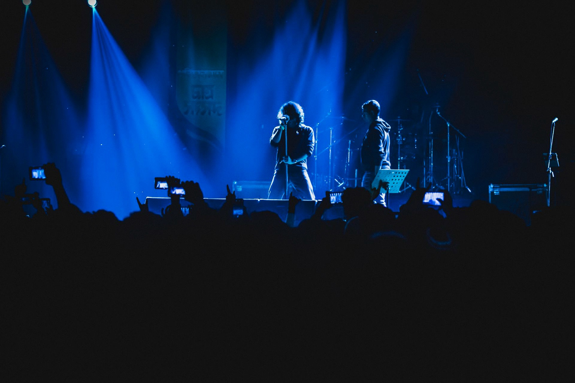 A singer at the mic in blue light, phones raised along the barrier